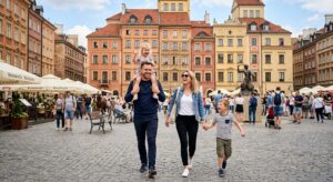 A high-quality editorial shot of a joyful family walking through Warsaw's Old Town square on a sunny