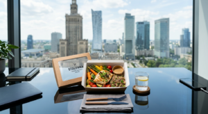 A top-down editorial shot of a gourmet takeaway lunch container on a sleek glass desk in a modern Wa